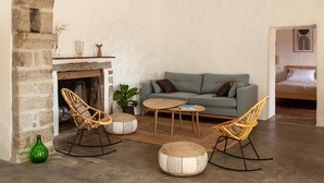 A cozy living room with a stone fireplace, a green sofa, two rocking chairs, and a small round table.