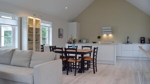 Cocina moderna con armarios blancos, microondas y un lavamanos. Hay un comedor con mesa y sillas de madera, y un sofá en la sala de estar.