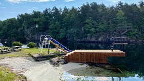 Un muelle de madera que se adentra en un lago, con un tobogán y una escalera que lleva a una plataforma.