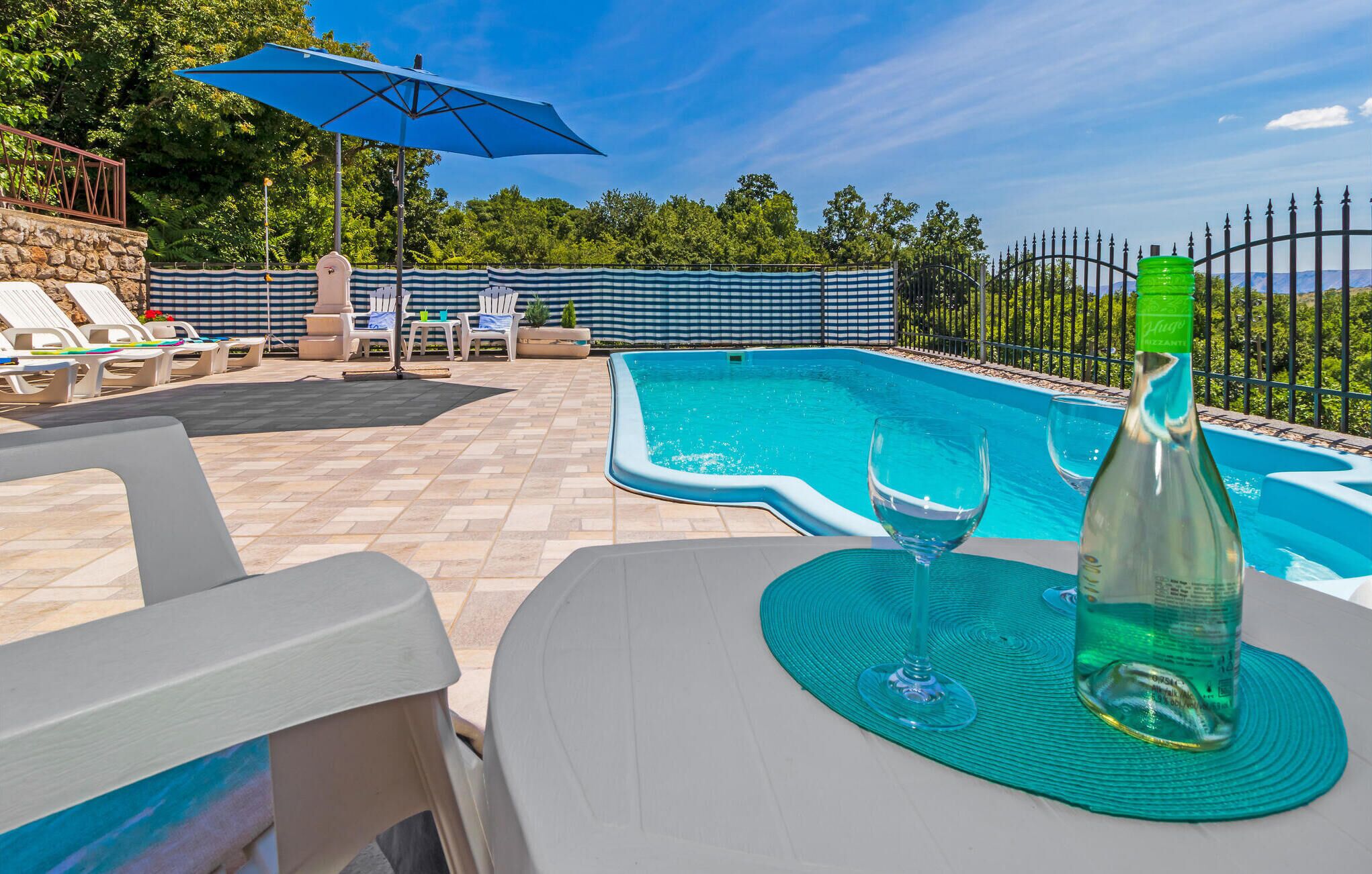 An outdoor swimming pool with lounge chairs and a table with a bottle and glasses.
