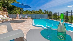 Una piscina exterior con sillas de descanso y una mesa con una botella y vasos.