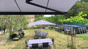 An outdoor patio with a table and chairs, a grill, and a shaded area.