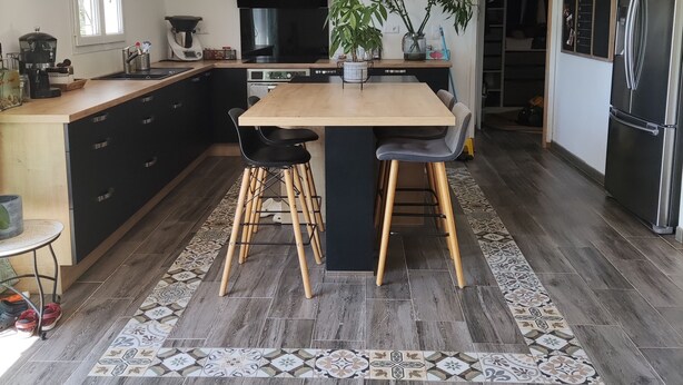 A modern kitchen with a central island, black cabinets, a large stove, and a refrigerator.