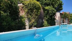 A clear blue swimming pool with a tiled edge, surrounded by greenery and a stone wall.