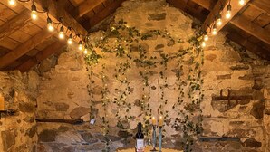 Una estança rústica amb parets de pedra i una taula de fusta preparada per a dues persones, decorada amb herba viva i llums de corda.