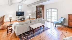 A living room with a wooden floor, a striped sofa, a television, a cabinet, and a large window. - Stunning home in Laurens (Laurens)