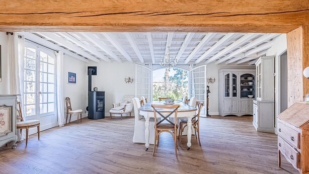 A spacious dining area with a high ceiling and exposed wooden beams, a large window with a view of trees, and traditional furniture. - Stunning home in Laurens (Laurens)