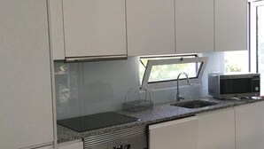 A modern kitchen with white cabinets, a built-in oven, a microwave, and a window above the sink. - Casa Modular T2 (Quelfes)