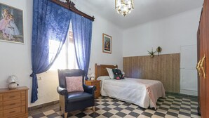 Ein Schlafzimmer mit kariertem Boden, einem Bett mit Holz-Kopfteil, einem schwarzen Ledersessel, einem Nachttisch mit Lampe und einem Fenster mit blauen Vorhängen.
