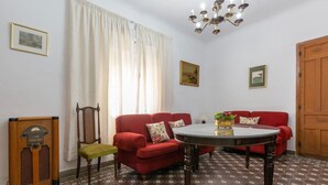 Ein Zimmer mit einem roten Sofa, einem Holzstuhl, einem Tisch mit Pflanze und einem Vintage-Radio.