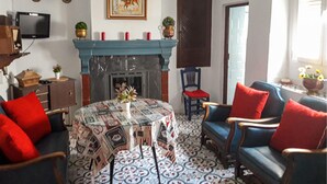 Ein Wohnzimmer mit Kamin, einem runden Tisch mit Zeitungen und zwei blauen Sesseln mit roten Kissen.
