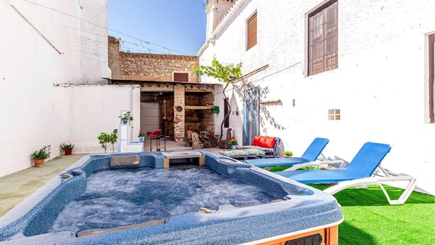 Ein Whirlpool in einem Innenhof mit Liegestühlen, einem kleinen Tisch und Topfpflanzen.