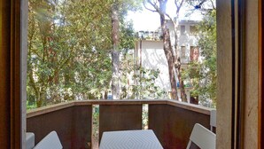 A balcony with two white wicker chairs and a table, overlooking a residential area with trees and buildings. - Beach front apartment in Rosolina Mare (Rosolina Mare)