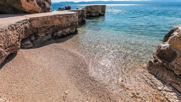 A rocky shoreline with clear water, a stone wall, and distant mountains. - 1 bedroom stunning apartment in Pisak (Pisak)