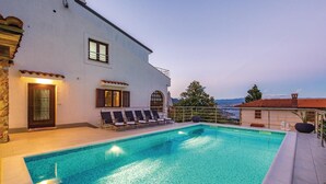 A swimming pool with lounge chairs, a stone wall, and a view of the sea. - Awesome Home in Lovran With Wifi and 6 Bedrooms (Lovran)