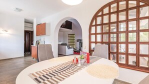 A modern living room with a round table, a large arched window, and a kitchen in the background. - Awesome Home in Lovran With Wifi and 6 Bedrooms (Lovran)