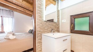 A bedroom with a bed, a bathroom with a sink and mirror, and a window with curtains. - Awesome Home in Lovran With Wifi and 6 Bedrooms (Lovran)