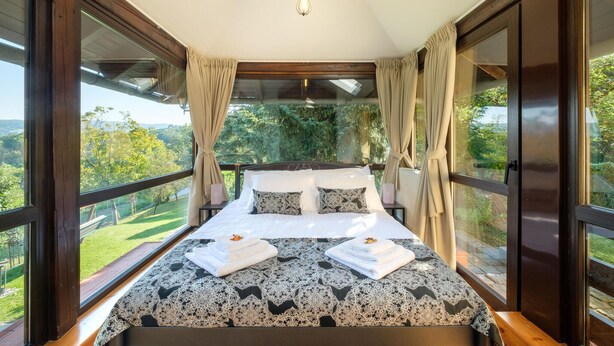 Ein Schlafzimmer mit einem großen Bett, Vorhängen und Blick auf Grünflächen.