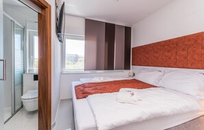 A modern hotel room with a large bed, a window with blinds, a flat-screen TV mounted on the wall, and a toilet with a modern design. - 2 bedroom cozy home in Sukosan (Sukosan)