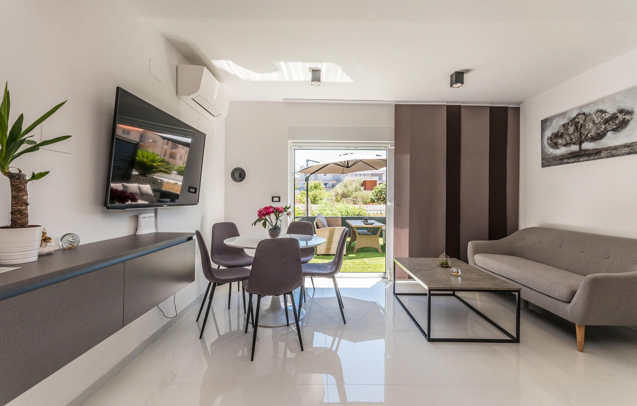 A modern living room with a flat-screen TV, a sofa, a coffee table, and a dining area with chairs and a table.