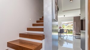 Una escala moderna de fusta que condueix a una zona d'estar oberta i lluminosa, amb una taula i cadires per dinar.