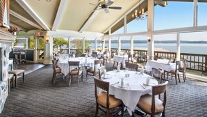 A restaurant with round tables and chairs, large windows, and a view of the water. -  Beautiful Abbey Springs Gated Golf Cart Community with Beach, Pools, & Golf (Fontana-on-Geneva Lake)