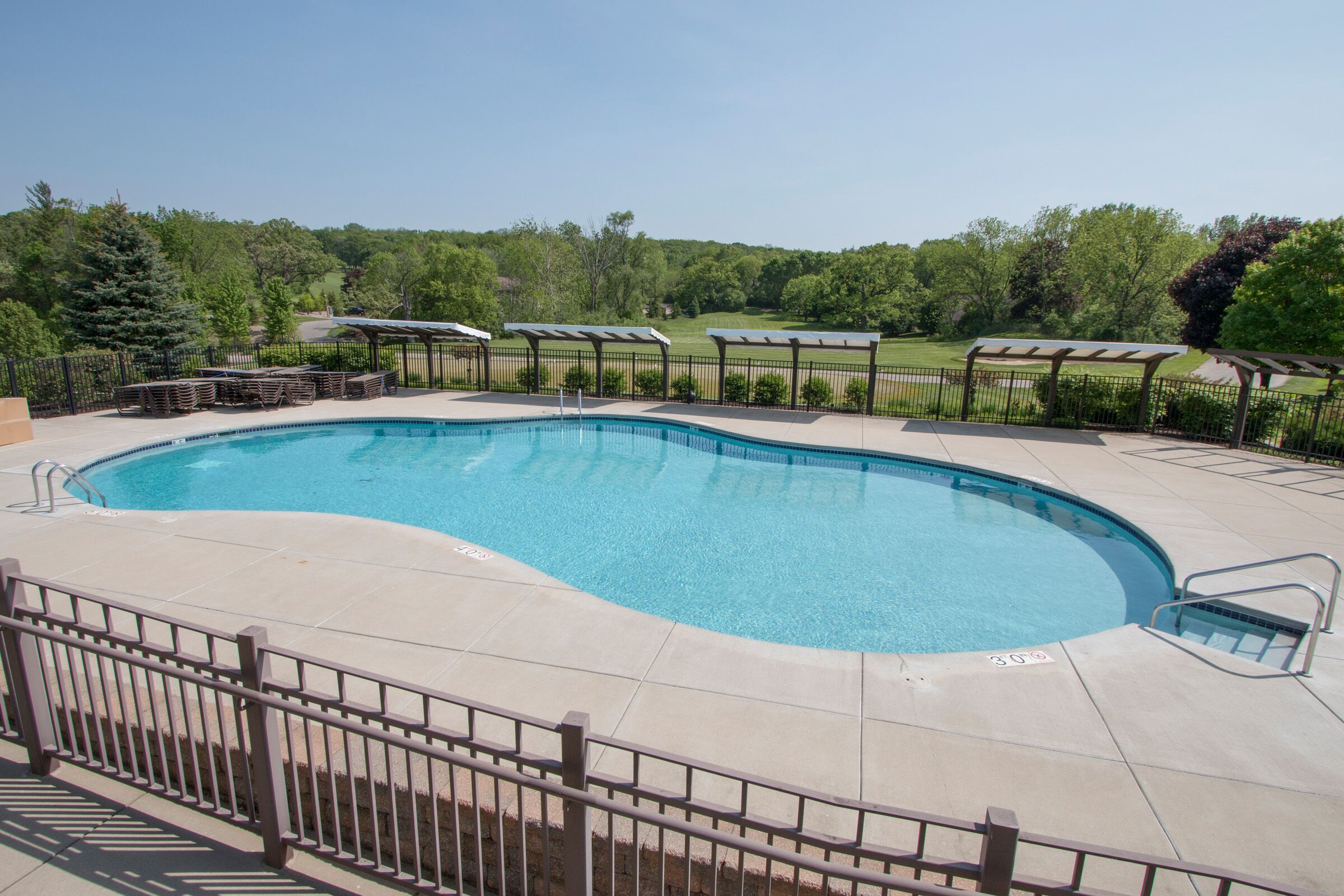 A rectangular swimming pool with a curved edge, surrounded by a metal fence and a paved deck.