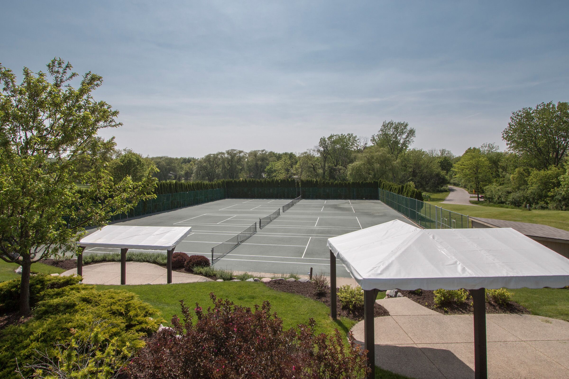 Un court de tennis entouré de verdure et doté d’un espace de repos couvert.