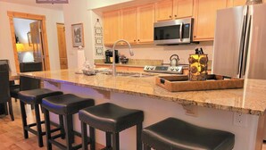 A kitchen with wooden cabinets, a stainless steel refrigerator, a microwave, a sink, and a bar stool seating area. - Downtown Fun! A/C shufflebrd Pacman, Steps Fm SkiBus, DogOK, walk to Yampa River (Steamboat Springs)