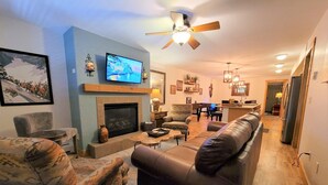 A living room with a fireplace, a television, a ceiling fan, and a dining area with a piano. - Downtown Fun! A/C shufflebrd Pacman, Steps Fm SkiBus, DogOK, walk to Yampa River (Steamboat Springs)