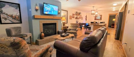 A living room with a fireplace, a television, a ceiling fan, and a dining area with a piano.