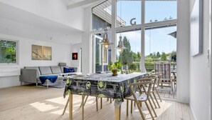Un grand espace de vie avec une grande fenêtre, une table à manger avec des chaises, un canapé et une plante en pot.