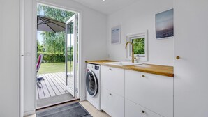 Une cuisine compacte dotée d’un lave-linge intégré, d’un plan de travail en bois et offrant une vue sur le jardin grâce à une porte vitrée.