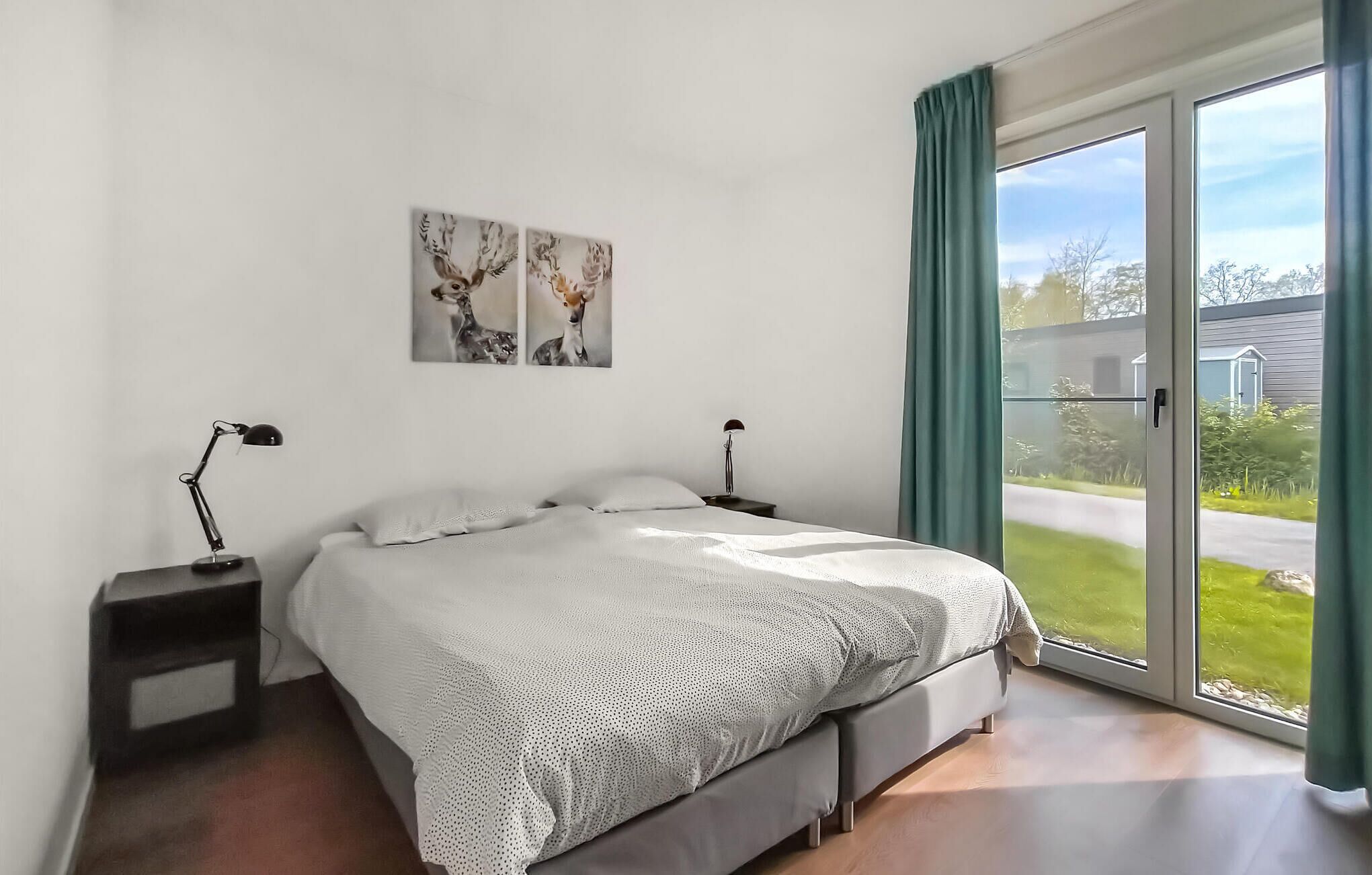 Quarto com cama, duas mesas de cabeceira, janela com cortinas e duas obras de arte na parede.