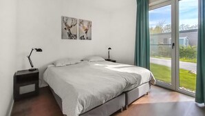 A bedroom with a bed, two bedside tables, a window with curtains, and two wall-mounted artworks.
