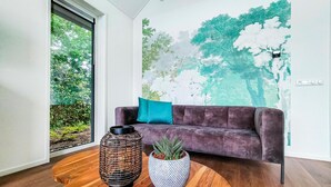 A modern living room with a dark purple sofa, a teal throw pillow, and two potted plants on a wooden coffee table.