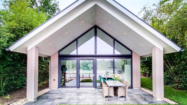 A modern house with a triangular roof, large glass doors, and a patio with outdoor furniture.