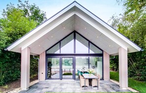 Een modern huis met een puntdak, grote glazen deuren en een terras met tuinmeubilair.