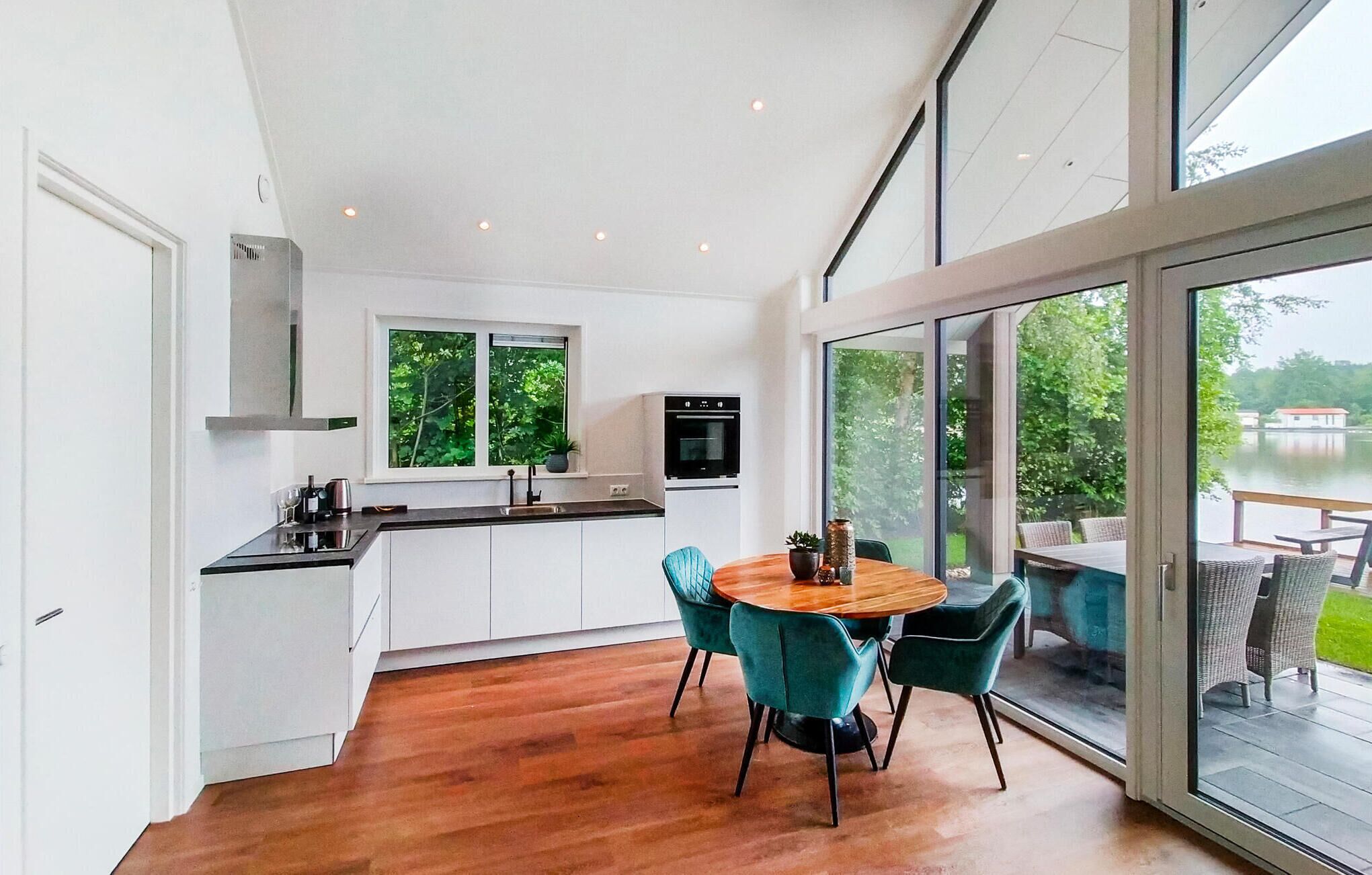 Une cuisine moderne avec des meubles blancs, un four noir et une fenêtre donnant sur un espace verdoyant.