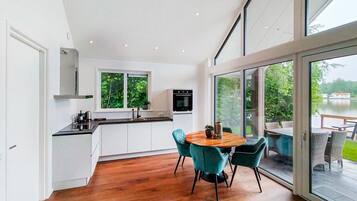 Une cuisine moderne avec des meubles blancs, un four noir et une fenêtre donnant sur un espace verdoyant.