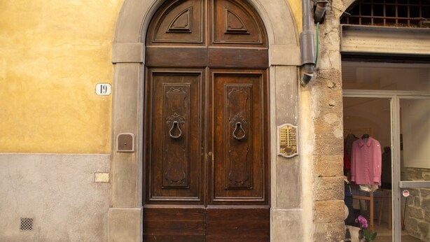 A double wooden door with a number plaque, a stone wall, and a shop window with a mannequin. - Bardi Suite apartment near Ponte Vechhio by Mmega (Firenze)