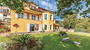 A two-story yellow building with balconies, a garden with various plants, and a stone wall. - Stunning Home in Icici With Wifi and 2 Bedrooms (Opatija)