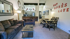 A cozy living room with a sofa, a coffee table, and a dining area with a wooden table and chairs. A kitchen is visible in the background. - Luxury Condo w/ FREE WiFi, Parking, Heated Pool, Hot Tubs, Skier Shuttles (Avon)