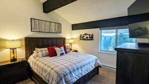 Un dormitorio con cama, dos mesitas de noche, una ventana con vistas y una obra de arte colgada en la pared.