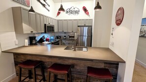Cozinha moderna com armários cinza, eletrodomésticos de aço inoxidável e uma ilha central com banquetas.