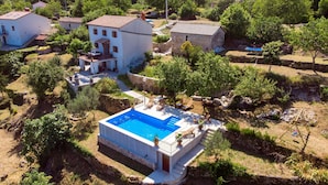Una villa con piscina, rodeada de exuberante vegetación y edificios de piedra.