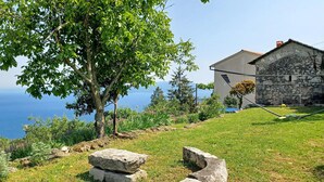 Un edificio de piedra con vista al mar, rodeado de césped y árboles.