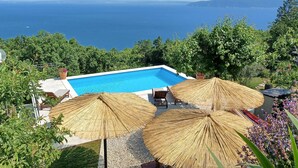 Una piscina con vistas al mar, rodeada de vegetación y algunas sombrillas.