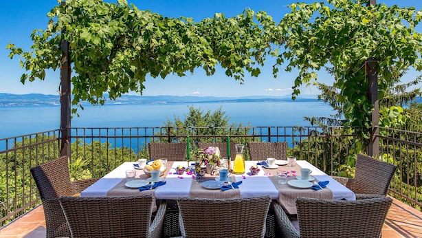 Una mesa para cuatro con sillas de mimbre, con vista a un cuerpo de agua y montañas.