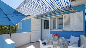 A patio with a table set for two, white chairs, and a striped awning providing shade. - Nice Apartment in Kosljun With Wifi and 1 Bedrooms (Pag)